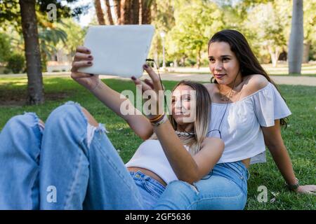 Jeune femme avec une amie qui prend le selfie à travers une tablette numérique au parc Banque D'Images