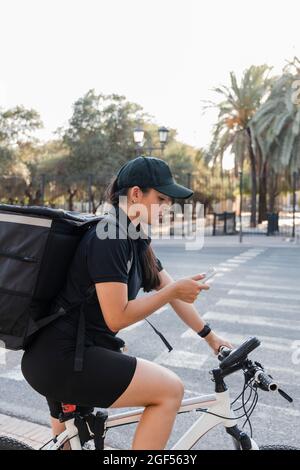 Jeune femme de livraison utilisant le téléphone portable tout en étant assis sur le vélo Banque D'Images