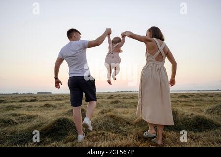 Parents balançant fille en marchant sur le terrain Banque D'Images