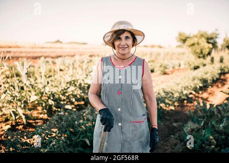 Une agricultrice âgée portant un chapeau lorsqu'elle est debout à la ferme maraîchère Banque D'Images