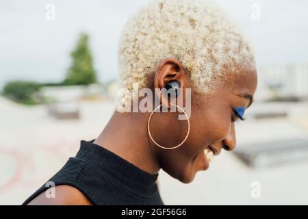 Jeune femme souriante avec écouteurs intra-auriculaires sans fil au parc Banque D'Images