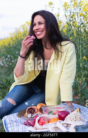 Femme souriante mangeant des fruits tout en étant assise dans le champ Banque D'Images