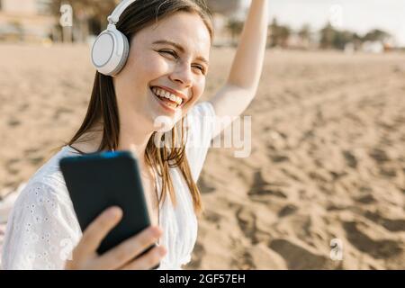 Bonne femme qui tient son téléphone mobile dansant tout en écoutant de la musique à travers des écouteurs à la plage Banque D'Images