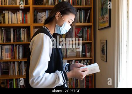 Une femme asiatique masquée par une pandémie naviguant dans une librairie Old Time Bricks and Mortar Banque D'Images