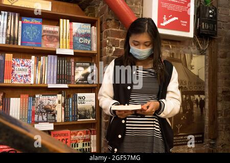 Une femme asiatique masquée par une pandémie naviguant dans une librairie Old Time Bricks and Mortar Banque D'Images