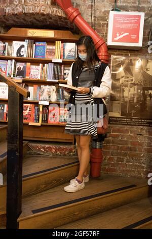 Une femme asiatique masquée par une pandémie naviguant dans une librairie Old Time Bricks and Mortar Banque D'Images