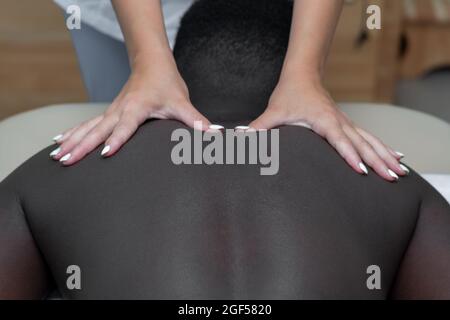 femme masseuse faisant le massage de la zone de l'épaule à l'homme noir Banque D'Images