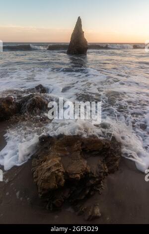 Un grand angle vertical avec des vagues de l'océan s'écrasant dans des rochers sur la plage et un grand rocher pointu au large de la côte dans l'eau Banque D'Images