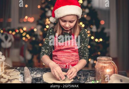 Petite fille dans le chapeau de père noël coupant des biscuits Banque D'Images