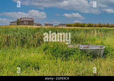 Petit bateau en aluminium au premier plan avec une maison abandonnée dans une cour de ferme des Prairies de la Saskatchewan, près du lac Rush, en Saskatchewan Banque D'Images