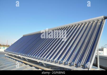 Un gros plan d'un système solaire d'eau chaude à tube sous vide, un collecteur de panneau solaire thermique installé sur un toit en métal contre le ciel bleu. Banque D'Images