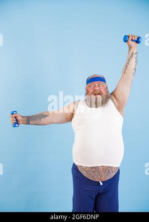 L'homme obèse choqué fait des exercices avec des haltères d'entraînement dur en studio Banque D'Images