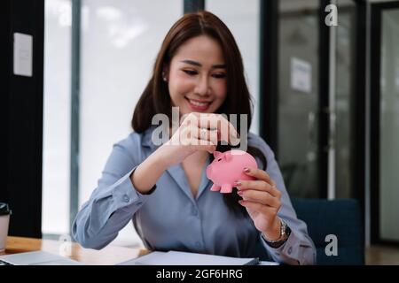 Gros plan main de la beauté asiatique femme mettant la pièce d'argent dans la banque porggy rose pour économiser l'argent richesse et le concept financier Banque D'Images