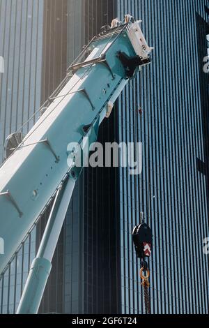 mécanisme de levage de grue bleue avec crochets près du bâtiment moderne en verre, grue et levage hydraulique haut jusqu'à 120 mètres. Banque D'Images