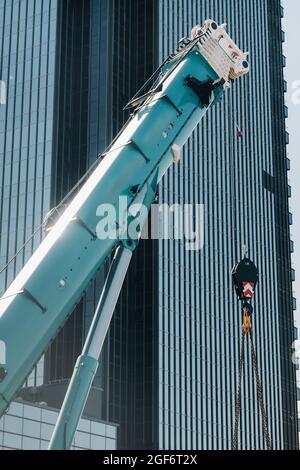 mécanisme de levage de grue bleue avec crochets près du bâtiment moderne en verre, grue et levage hydraulique haut jusqu'à 120 mètres. Banque D'Images