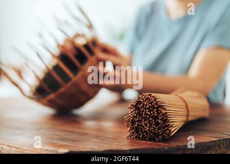 Femme tisse un panier de tubes en papier sur une table en bois Banque D'Images