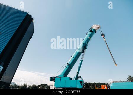 mécanisme de levage de grue bleue avec crochets près du bâtiment moderne en verre, grue et levage hydraulique haut jusqu'à 120 mètres. Banque D'Images