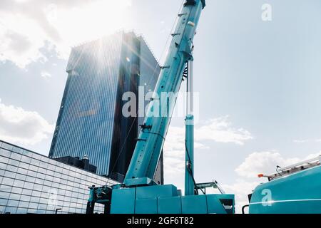 mécanisme de levage de grue bleue avec crochets près du bâtiment moderne en verre, grue et levage hydraulique haut jusqu'à 120 mètres. Banque D'Images