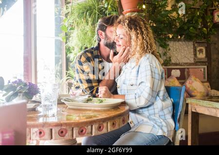 Couple caucasien adulte jeune dans l'amour et tendresse émotions assis ensemble au restaurant appréciant la relation - datant personnes matures embrassant un Banque D'Images