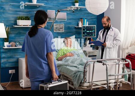 Infirmier soignant homme écrivant un traitement médicamenteux sur le presse-papiers discutant de l'aide médicale. Femme sénior au lit pendant les soins sociaux femme âgée à la retraite. Assistance technique Banque D'Images