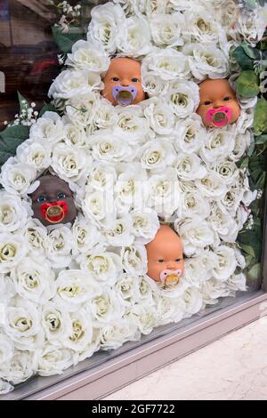 Un étrange, étrange, effrayant, drôle, inhabituel, vitrine de façade unique de décoration de fleurs blanches en plastique avec têtes de poupée bébé avec sucettes. Dans est Banque D'Images