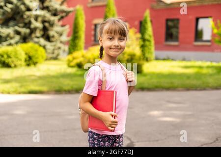 Retour à l'école. Concept d'éducation. Jolie fille souriante sur le chemin de l'école. Bonne petite fille enfant tenant les livres avec sac à dos. Banque D'Images