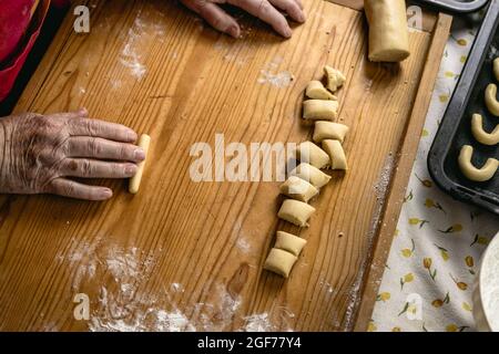 Moulage de croissants de vanille à partir de pâte à pâtisserie sur panneau de bois. Femme âgée qui cuit des biscuits de noël. Préparation de mets sucrés faits maison Banque D'Images