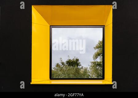 Fenêtre jaune sur façade noire avec reflet de l'arbre vert. Arrière-plan de l'architecture abstraite Banque D'Images