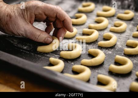 La femme âgée met des croissants de vanille sur la plaque de cuisson, comme vanillekipferl, en faisant des biscuits de noël traditionnels faits maison. Prêt pour la cuisson Banque D'Images