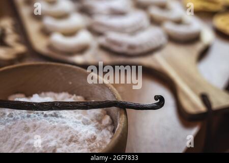 Cuisson avec une gousse de vanille ou une gousse de vanille. Bol en bois avec sucre et vanillekipferl. Petits gâteaux de Noël sur table Banque D'Images