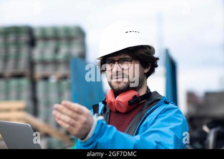 Jeune ingénieur portant un casque et une protection auditive sur un poste de travail extérieur sur un chantier de construction avec un ordinateur portable, Fribourg, Bade-Wurtemberg Banque D'Images