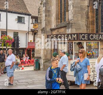 Une rue piétonne lors d'une journée bien remplie. Une remorque servant de la glace est placée à côté d'une église. Deux hommes mangent des glaces pendant que les gens marchent. Banque D'Images