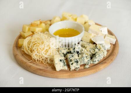 Planche en bois avec divers types de fromages et bol de miel, en-cas sain, concentration sélective Banque D'Images