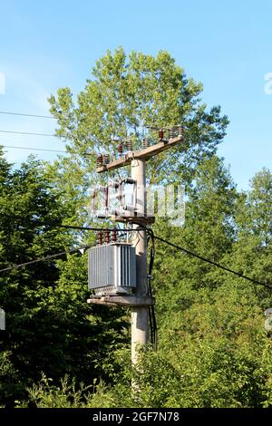 Transformateur électrique en métal gris avec isolateurs en céramique marron sur le dessus monté sur un poteau de service en béton Banque D'Images