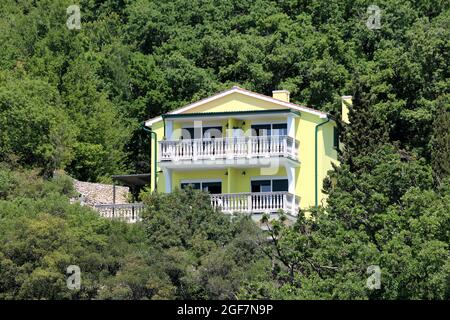 Nouvelle grande maison familiale suburbaine jaune avec deux balcons blancs allongés à l'avant et terrasse attachée construite sur le côté de la petite colline Banque D'Images