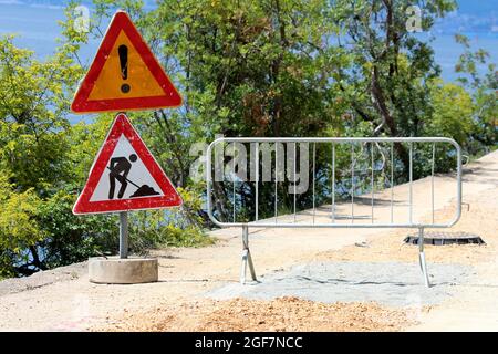 Début d'un chantier de construction de routes fermées avec deux routes d'avertissement en voie de délabrement très utilisées devant les panneaux de signalisation à côté de la clôture de protection en métal Banque D'Images