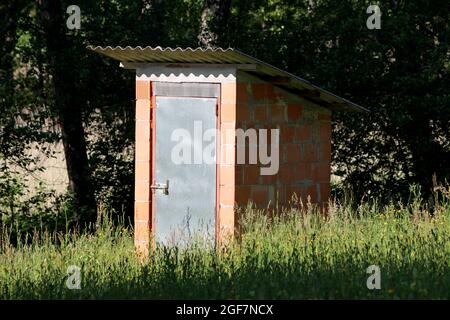 Petit hangar à outils de jardin fait maison, non fini, fait de blocs de construction rouges et fermé avec des portes métalliques verrouillées avec cadenas construit en banlieue Banque D'Images