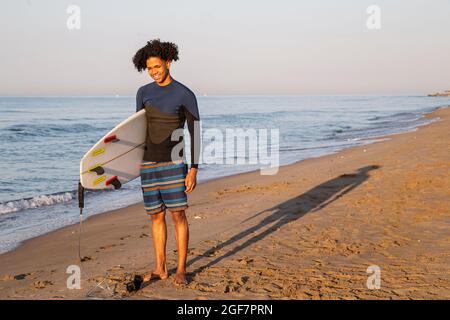 Photo d'un jeune surfeur souriant avec une planche de surf sur la plage. Banque D'Images