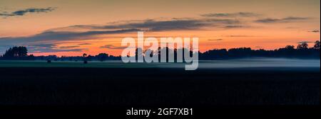 Un panorama de coucher de soleil et de nuit sur les champs de ferme et la forêt avec un faible brouillard rampant Banque D'Images