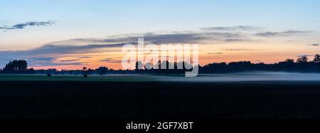 Un panorama de coucher de soleil et de nuit sur les champs de ferme et la forêt avec un faible brouillard rampant Banque D'Images