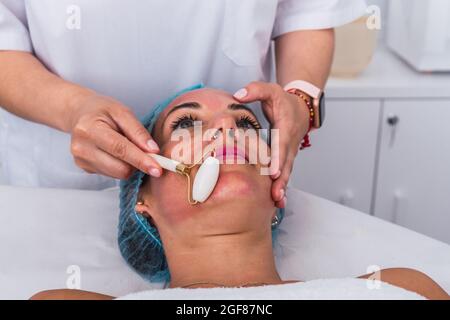 Cosmetologiste effectuant un massage avec un rouleau de jade à une femme au spa de beauté Banque D'Images