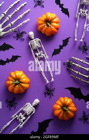 Joyeux Halloween concept de vacances. Pose plate, citrouilles à vue de dessus, squelettes, chauves-souris, araignées sur fond violet. Banque D'Images