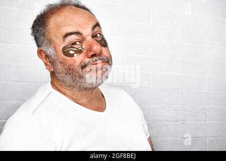 Beau charmant homme barbu aux cheveux gris avec des taches d'oeil hydrogel sur son visage. Soin de la peau pour hommes. Banque D'Images
