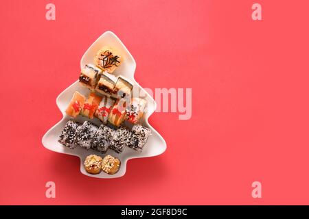 Sushi servi dans l'assiette comme arbre de Noël avec décoration de fête sur fond rouge. Vue de dessus. Banque D'Images