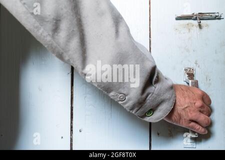 Homme main dans une chemise ferme une porte en bois avec une serrure, peinte en bleu, dans une ferme. Banque D'Images