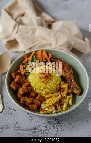 Plats indonésiens, nasi kuning ou riz curcuma, servis avec du tempeh, de l'urap ou des légumes avec une sauce à la noix de coco, des cuisses de poulet rôti et des œufs frits. Banque D'Images