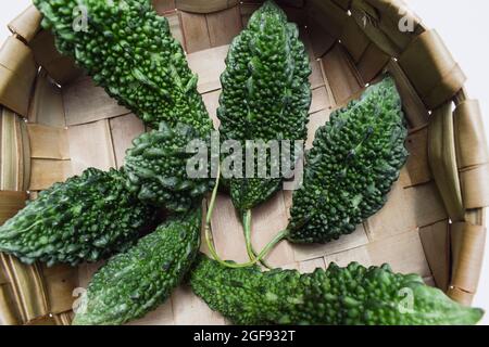 Bittergourd ou Bittermelons empilés dans le panier. Légumes verts différentes tailles de Karela dans un panier en osier avec fond boisé Banque D'Images