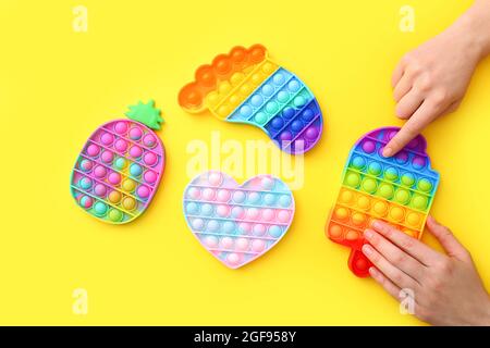Les jouets sensoriels antistress colorés que le violon pousse le pop sur fond jaune, vue du dessus Banque D'Images