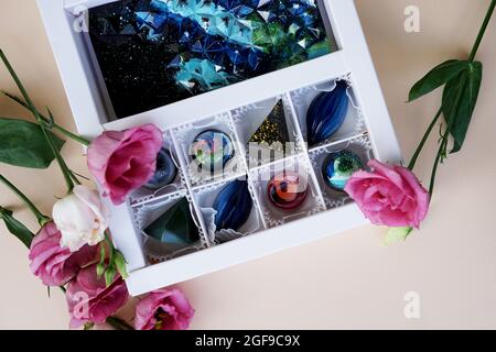 Un ensemble de bonbons faits main dans un emballage blanc de fête. Design de l'espace. Bonbons sur fond clair et décor de fleurs roses Banque D'Images