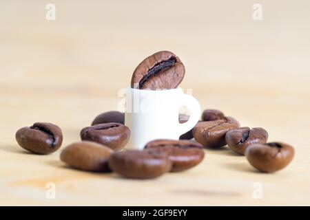 Petite tasse de café entourée de grains de café éparpillés sur fond marron clair. Le concept de consommation modérée. Banque D'Images